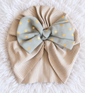 Beige ribbed baby turban with gray blue bow and gold polka dots on white rug