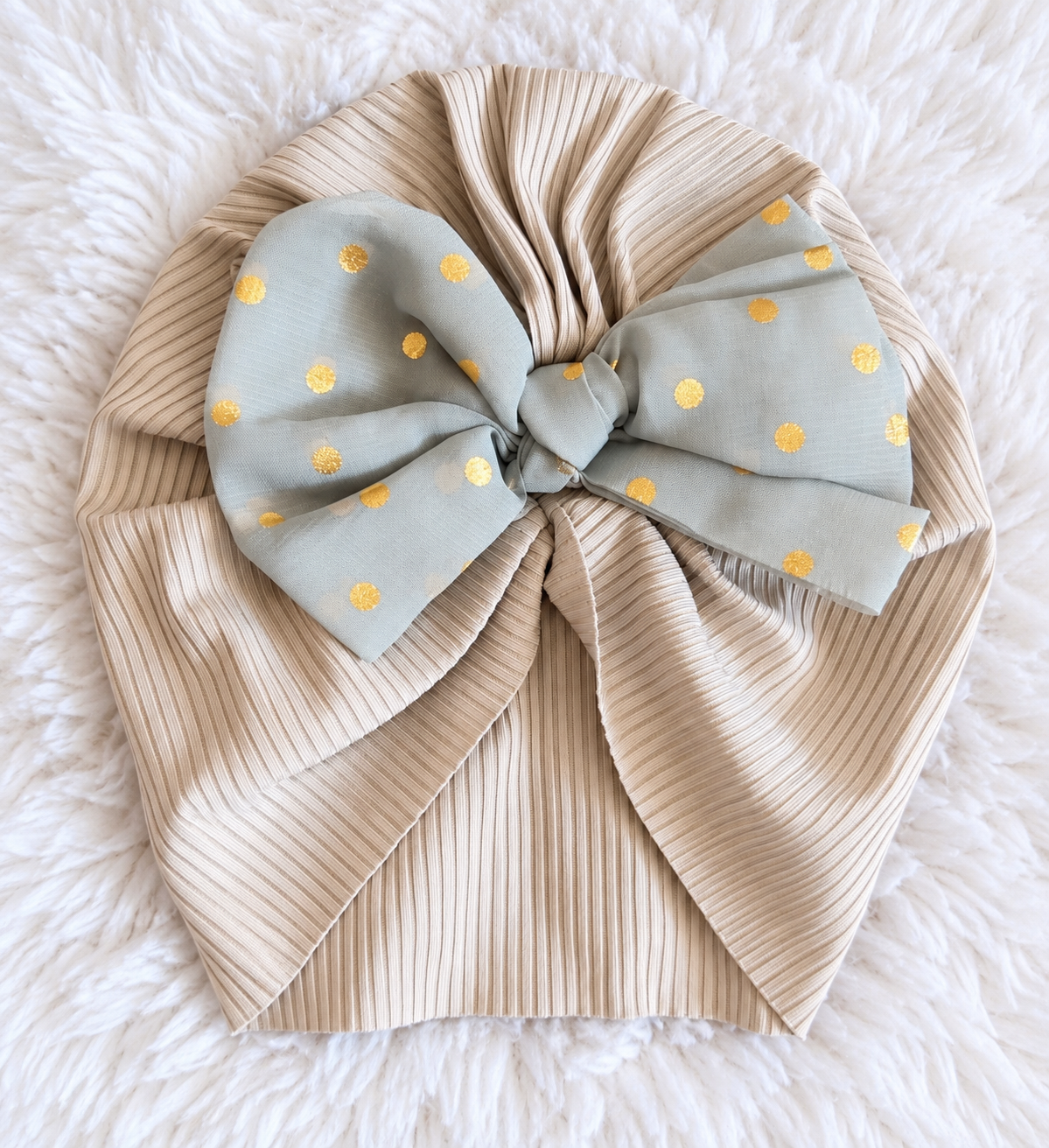 Beige ribbed baby turban with gray blue bow and gold polka dots on white rug