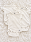 Three white Gerber ribbed flutter-sleeve bodysuits on a white rug