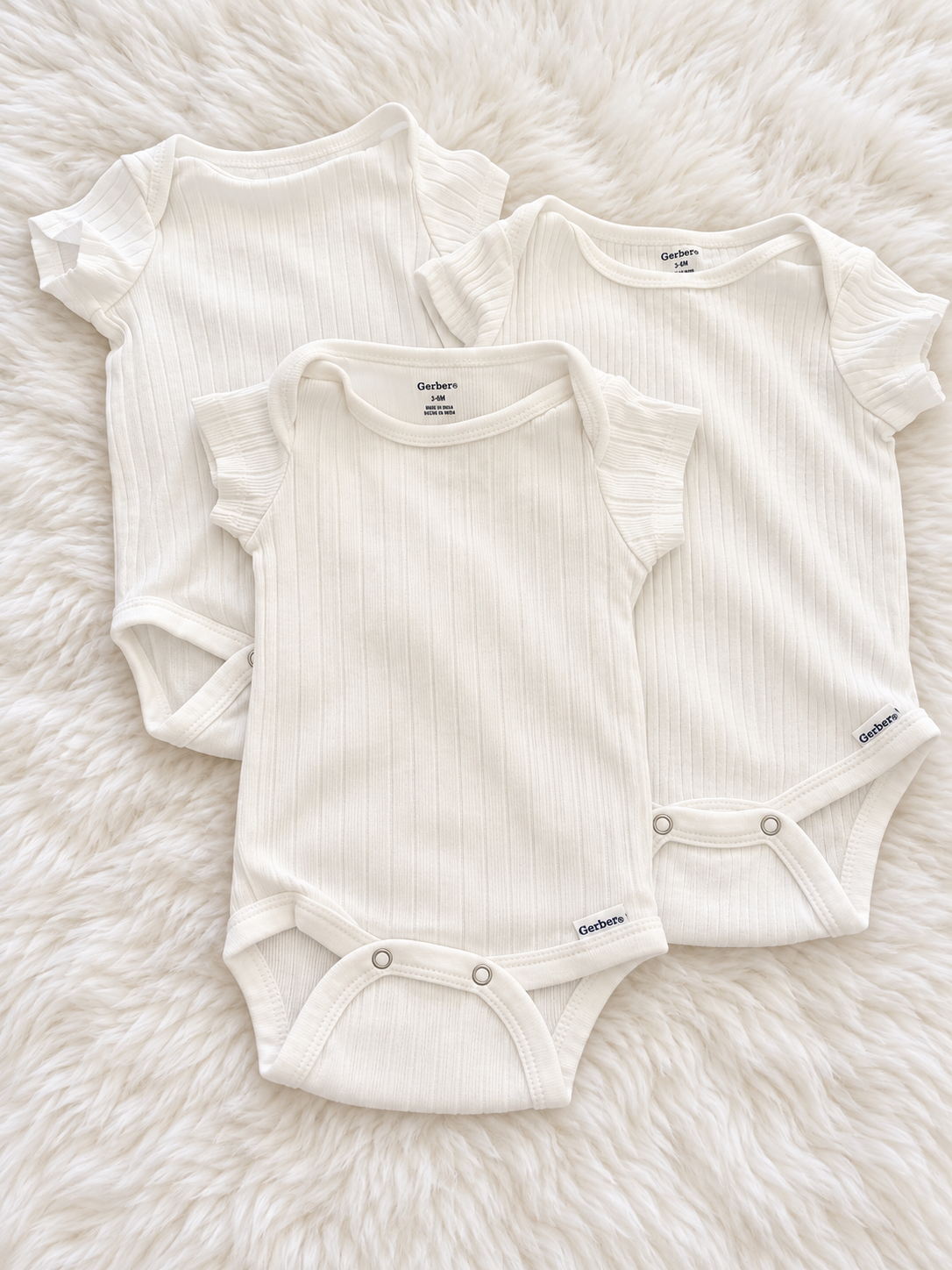 Three white Gerber ribbed flutter-sleeve bodysuits on a white rug