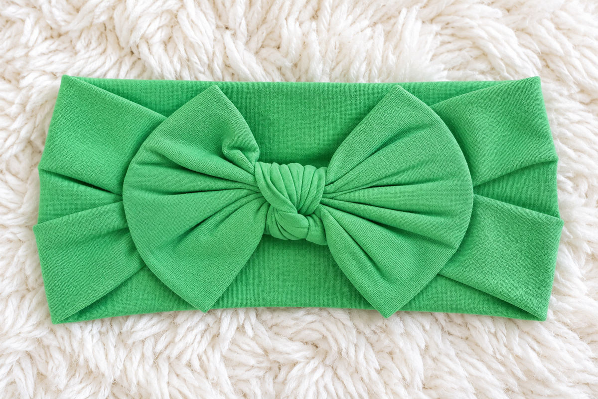 Green bow baby headband on white rug
