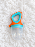 Orange and teal baby food feeder with clear cover on white rug