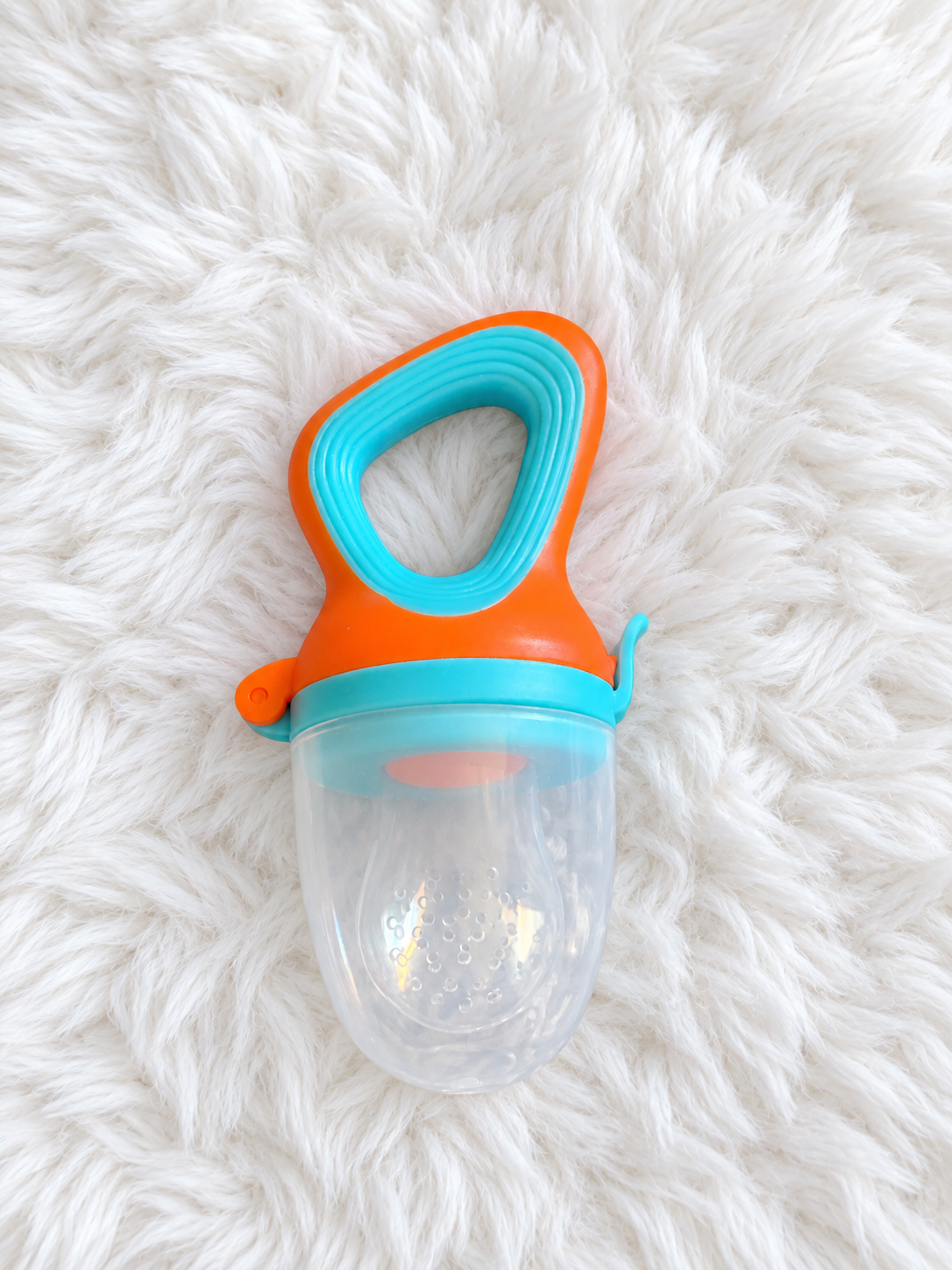 Orange and teal baby food feeder with clear cover on white rug