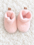 Pink fuzzy baby booties on white rug