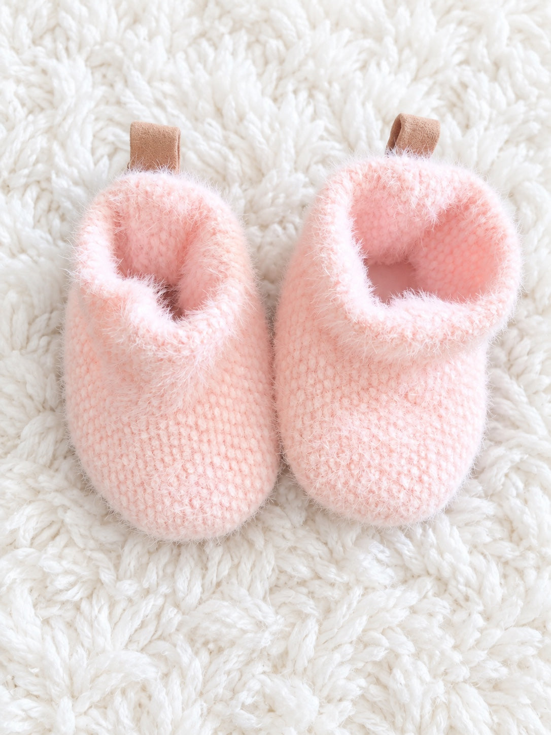 Pink fuzzy baby booties on white rug