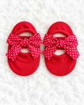 Red baby sock shoes with white polka dot bows on white rug background