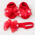 Red baby sock shoes and matching pom-pom bow headband on white rug