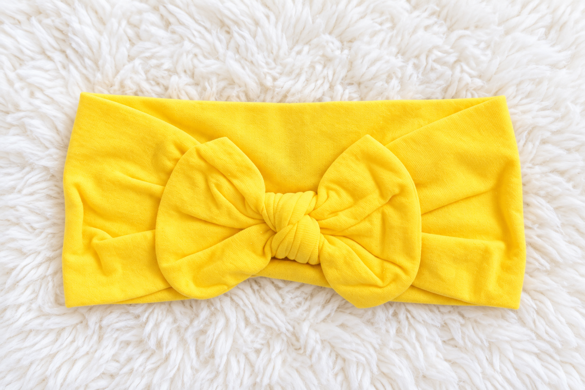 Bright yellow bow headband on a white rug